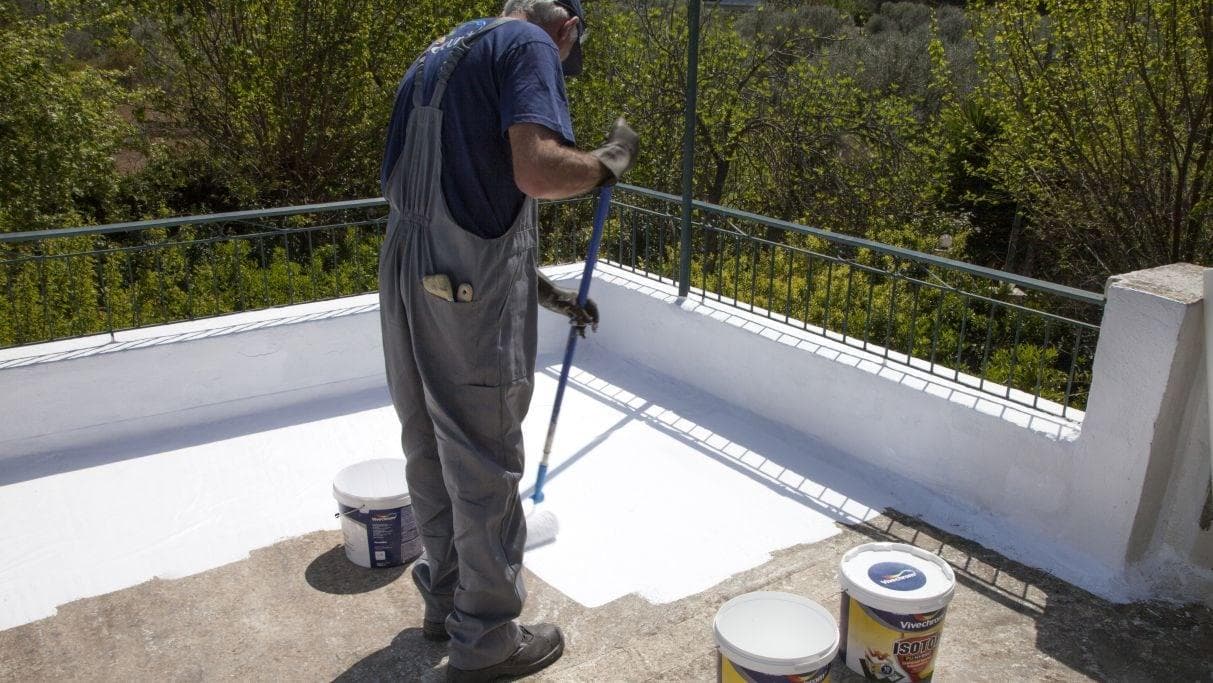 Worker applying white ISOTOP waterproofing paint on a terrace