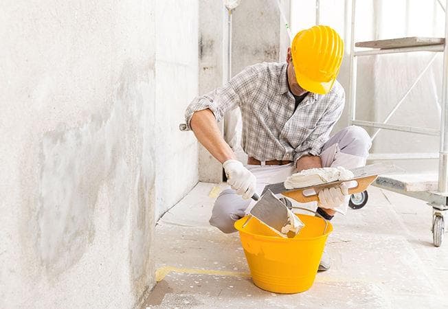 Technician preparing filler for wall damp repair indoors
