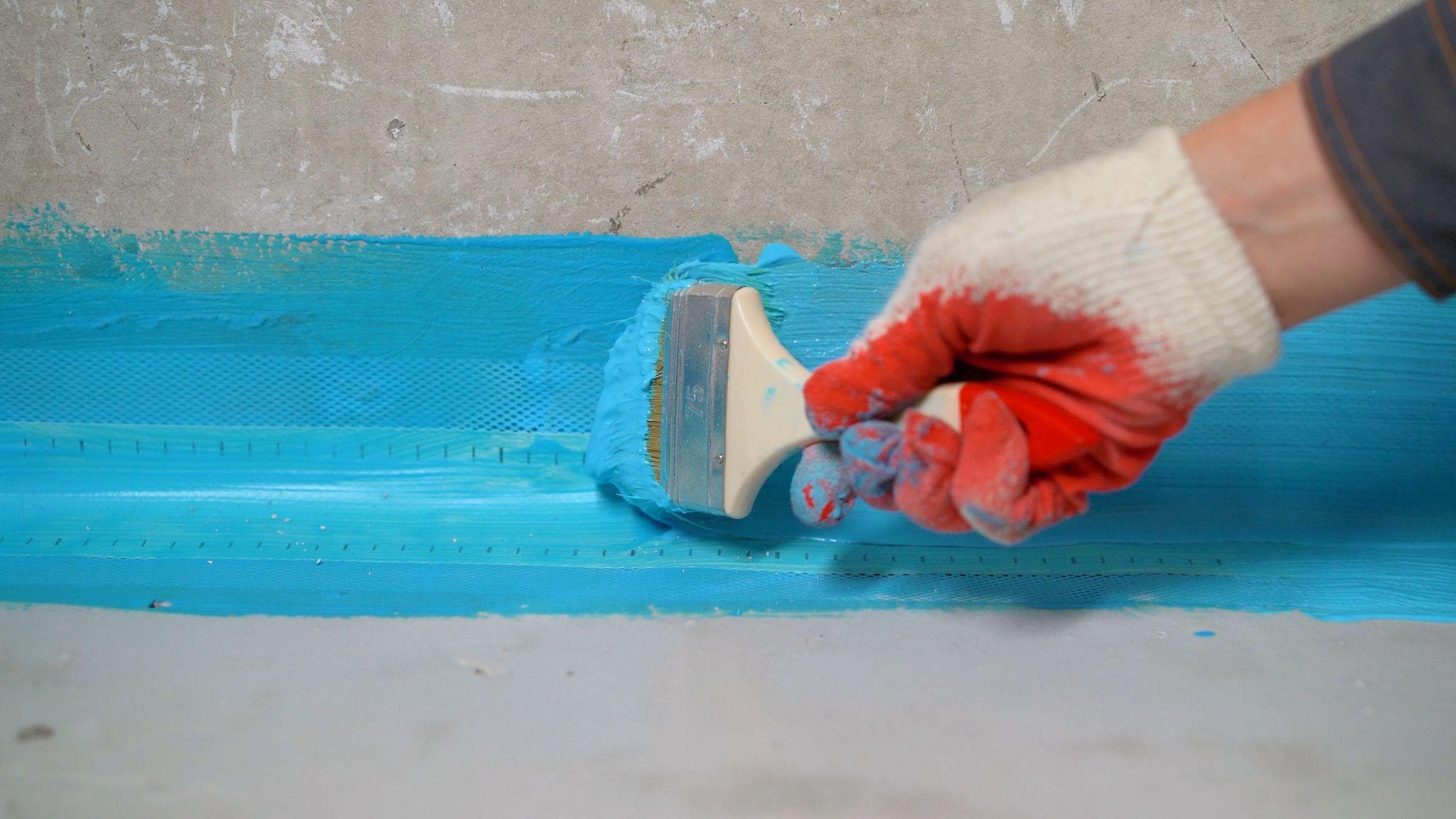 Blue waterproofing membrane brushed along a concrete wall and floor corner