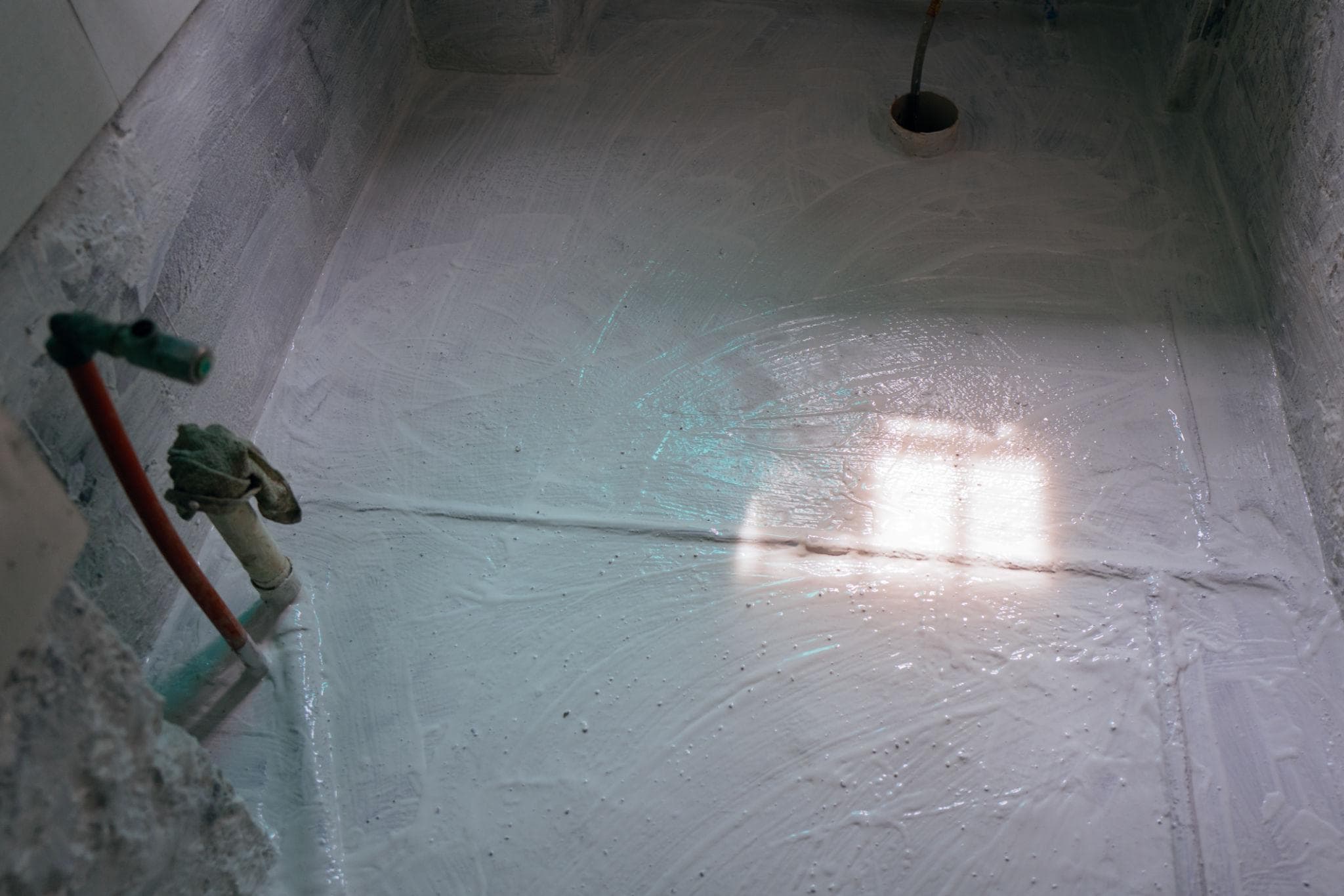 Fresh white waterproofing coat applied across a bathroom floor